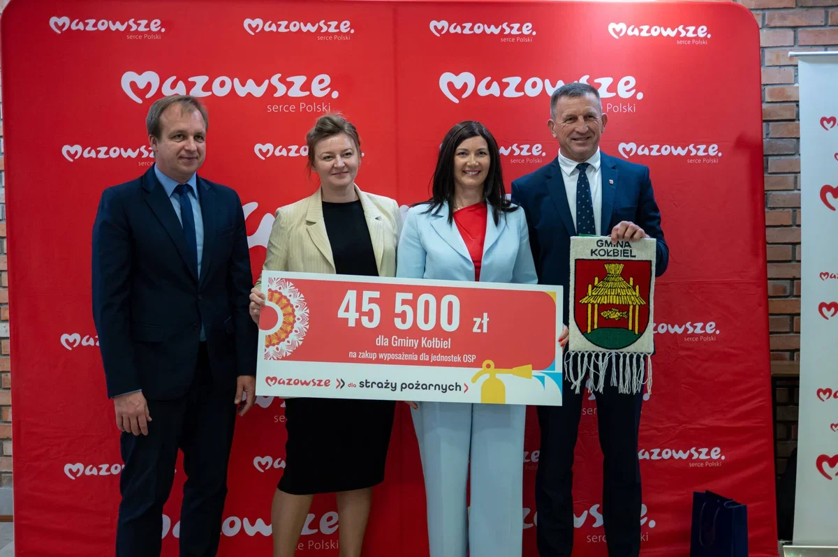 Cztery osoby stoją przed czerwoną ścianką z logotypem Mazowsze i trzymają czek na 45 500 zł dla Gminy Kotbiel na zakup wyposażenia dla jednostek OSP oraz gminow