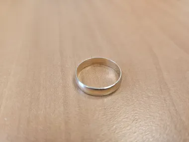 Złota obrączka leży na jasnobrązowej powierzchni drewnianego stołu.