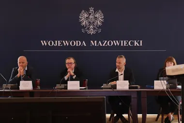 Cztery osoby siedzą za stołem konferencyjnym w sali z napisem „Wojewoda Mazowiecki” i orłem na ścianie.